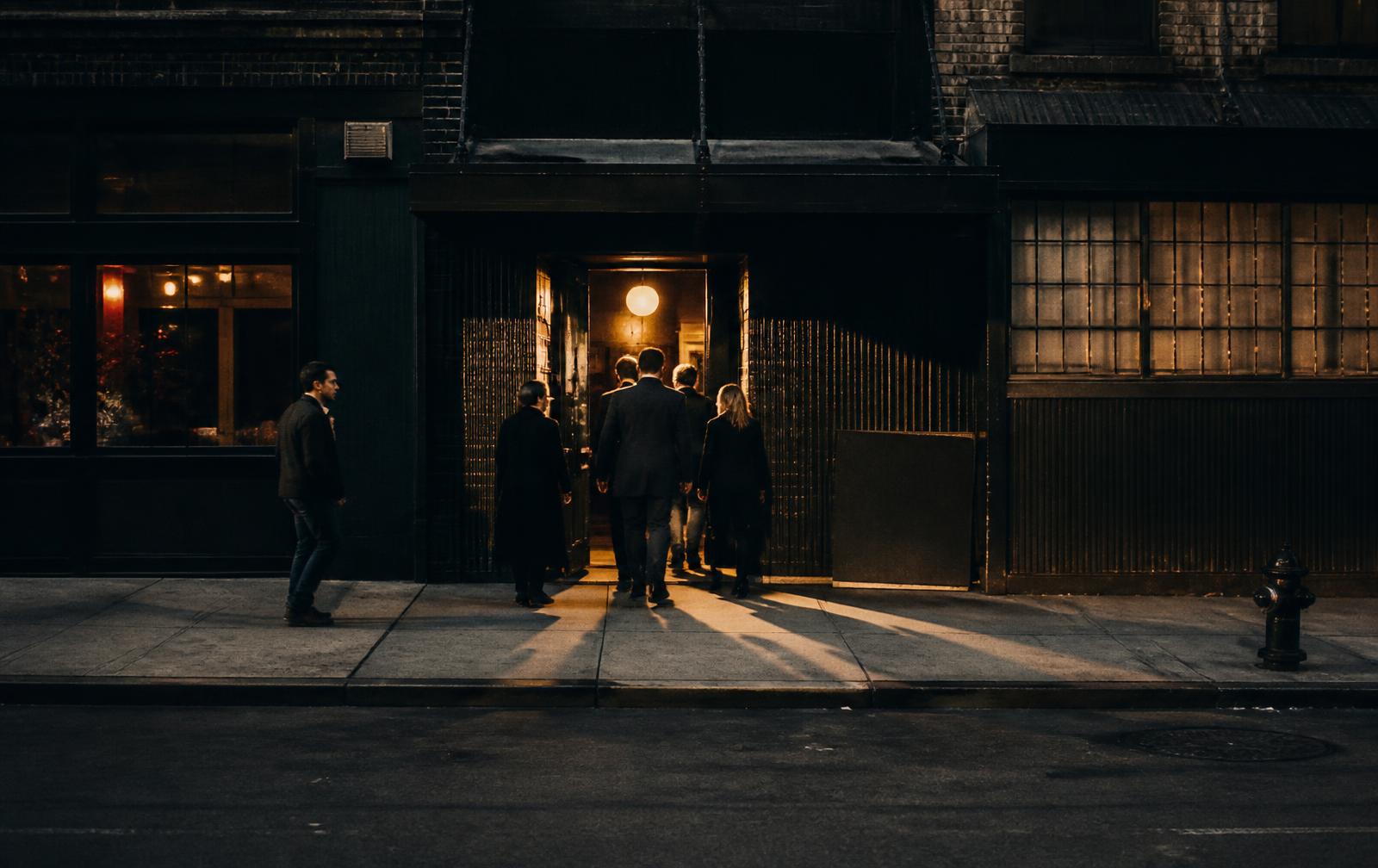 People entering a lit New York venue doorway at dusk